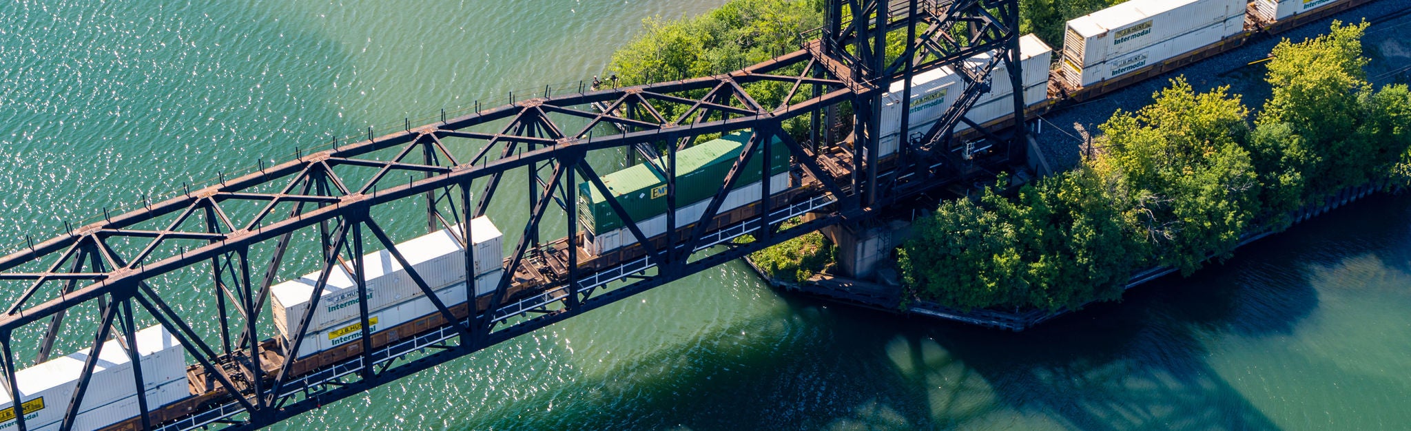 An aerial shot of an intermodal shipping train moving on a bridge over a river